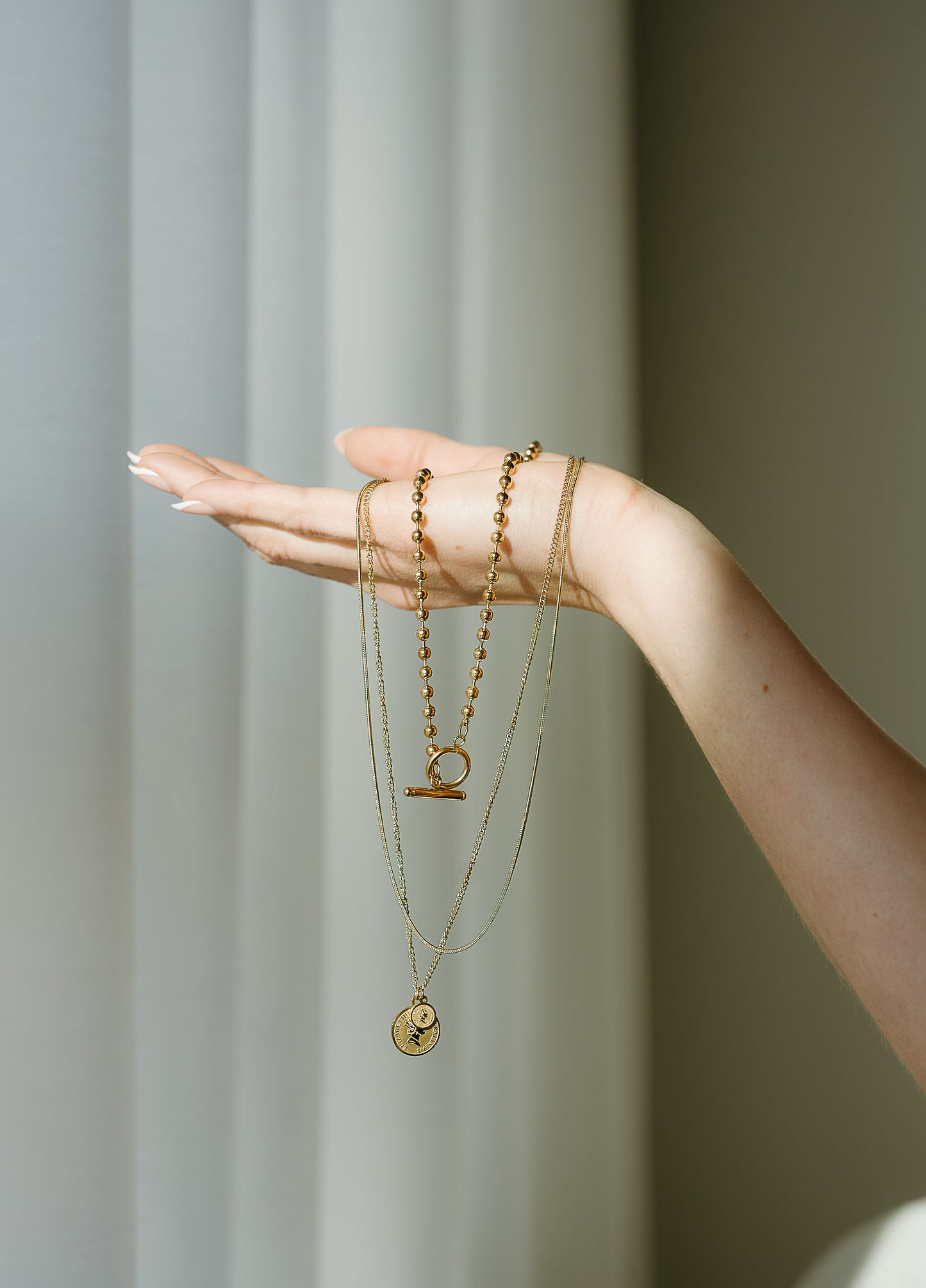 Hand wearing multiple gold necklaces against a neutral background