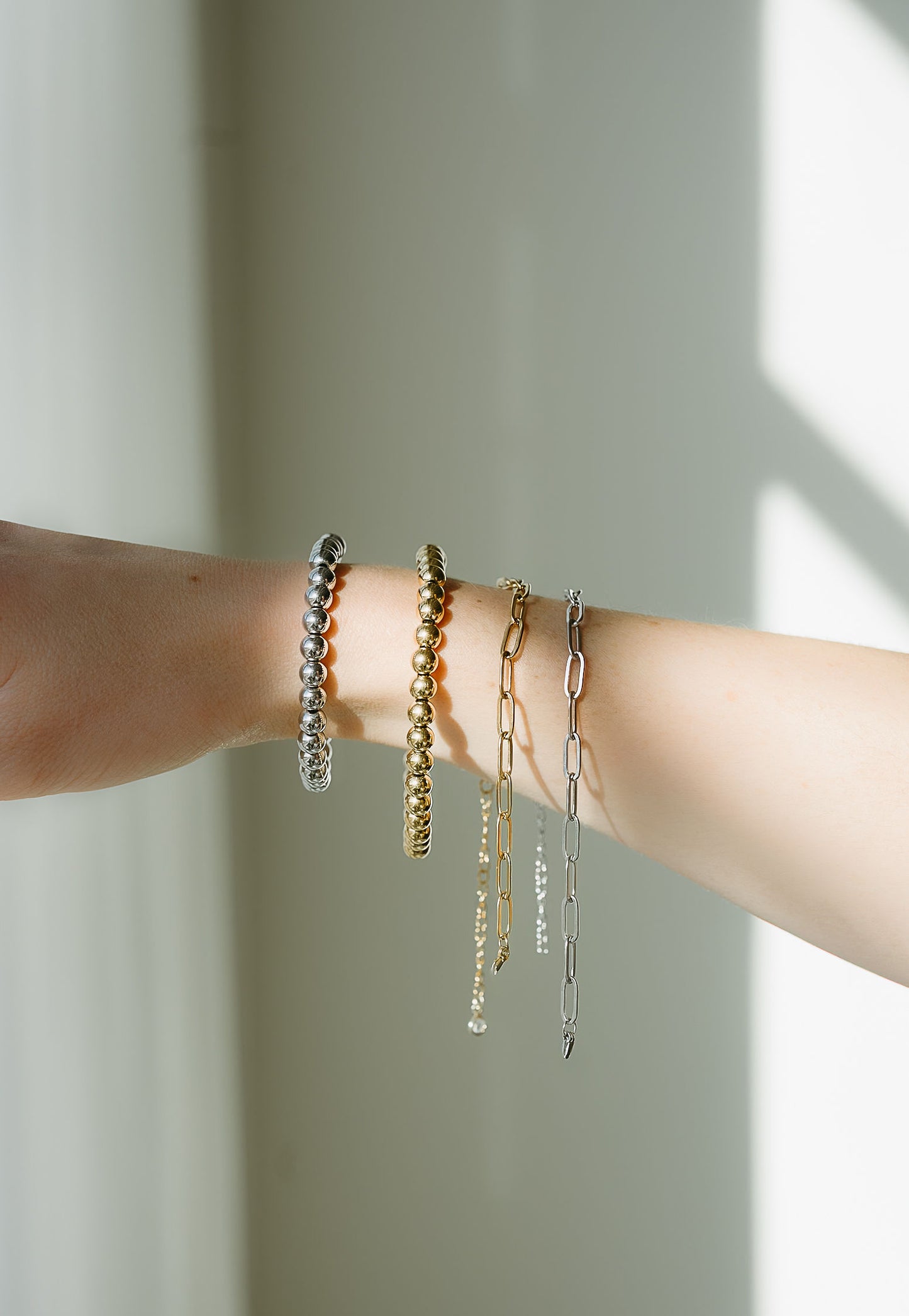 Close-up of a person's arm wearing multiple bracelets on a neutral background