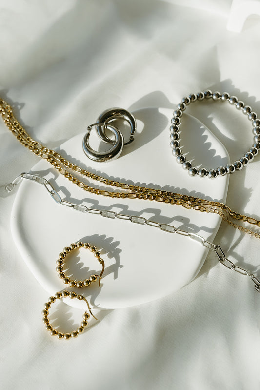 Gold and silver jewelry including necklaces and rings on a white fabric background