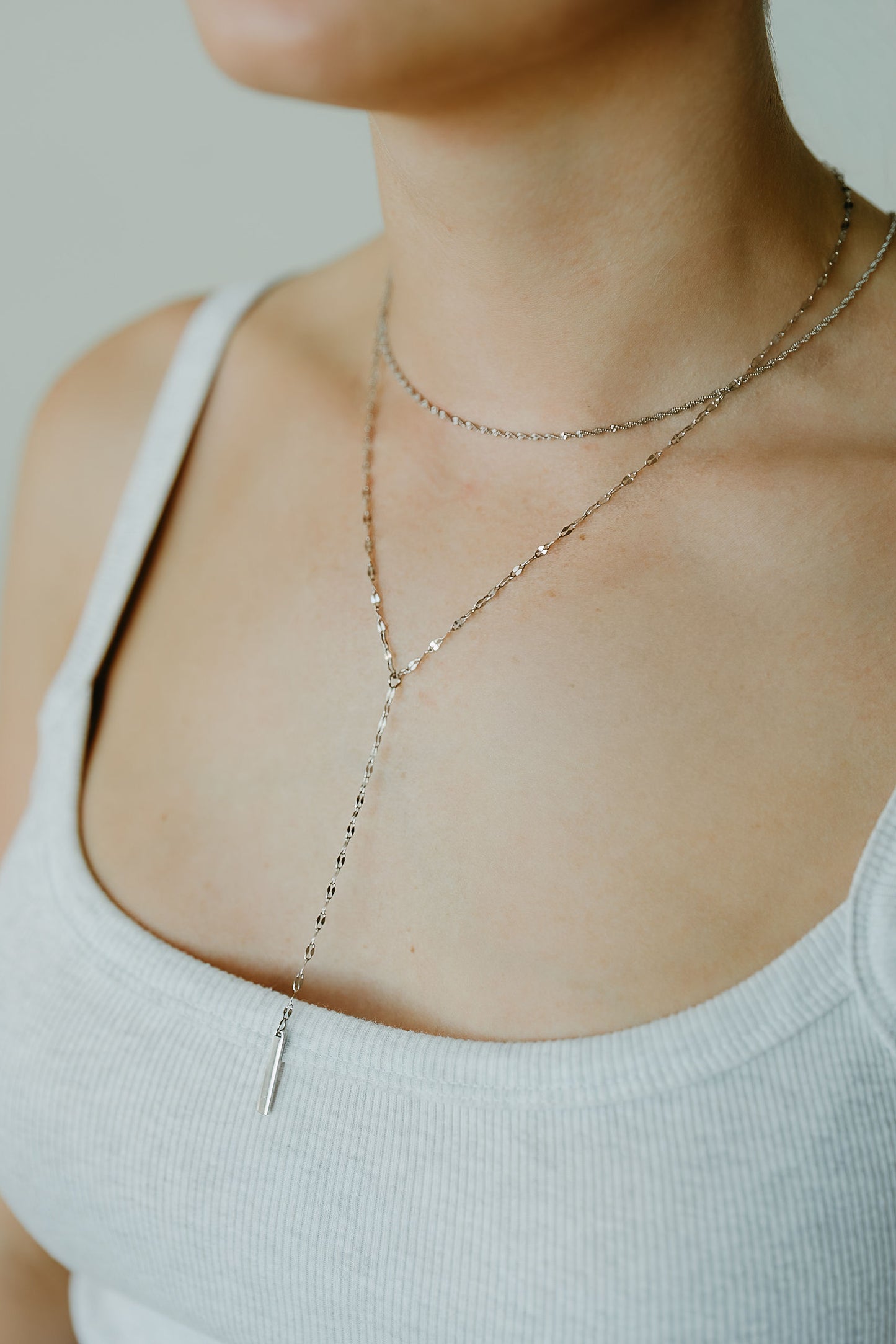 Close-up of a person wearing a delicate necklace with a neutral background