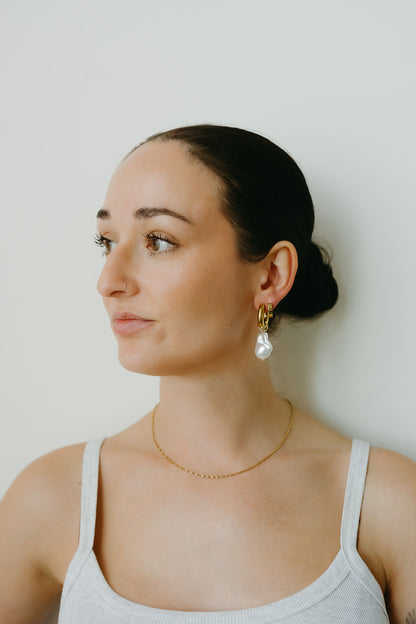 Woman wearing gold necklace and earrings against a plain background