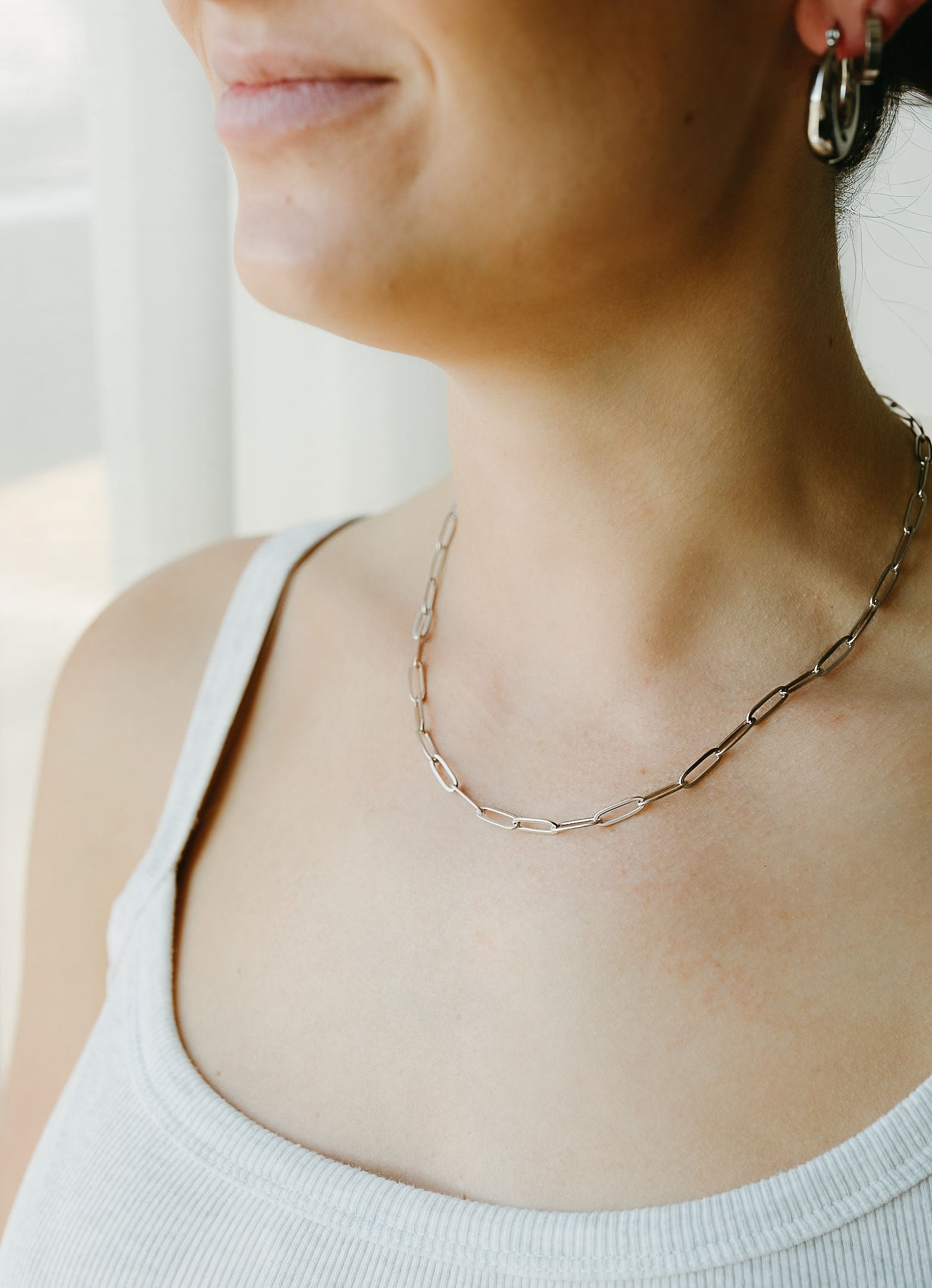 Close-up of a person wearing a delicate gold chain necklace and hoop earrings.