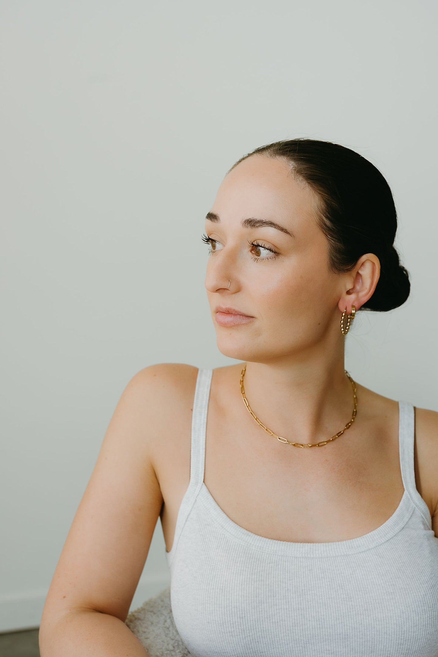 Woman wearing a white tank top and gold necklace against a plain background