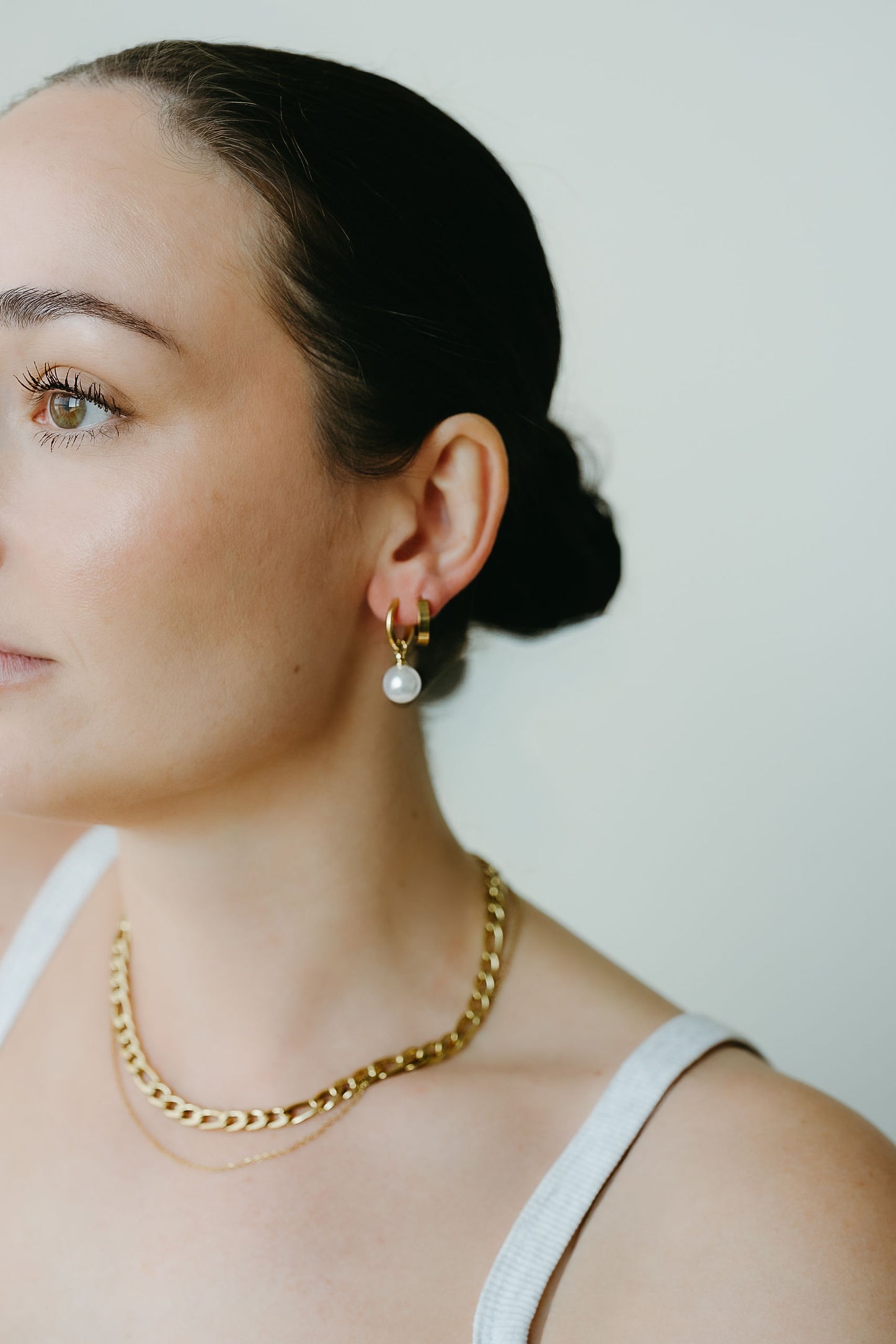 Woman wearing gold chain necklace and pearl earring against a plain background