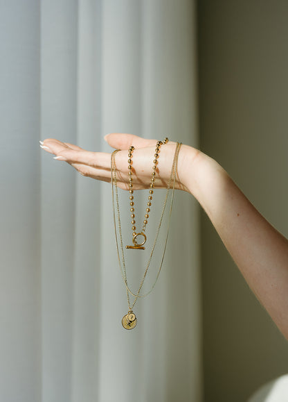 Hand wearing multiple gold necklaces against a neutral background