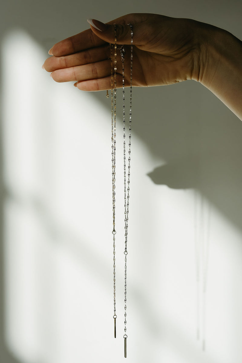 Hand holding a delicate chain necklace against a neutral background